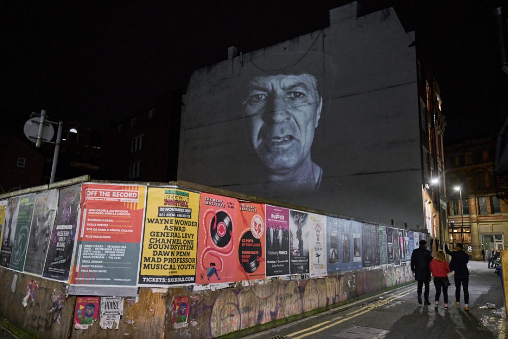 This image shows a portrait of a man that is being projected against a wall in a dis-used part of Manchester city centre.