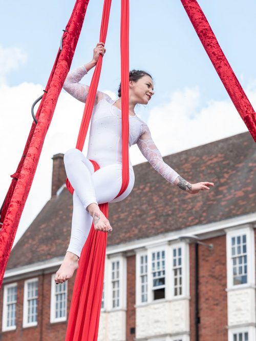 A lady is performing in red set of silks in a aerial performance.