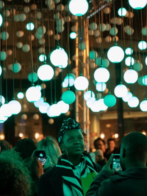 Audiences standing within a light installation of glowing light bulbs, taking pictures.