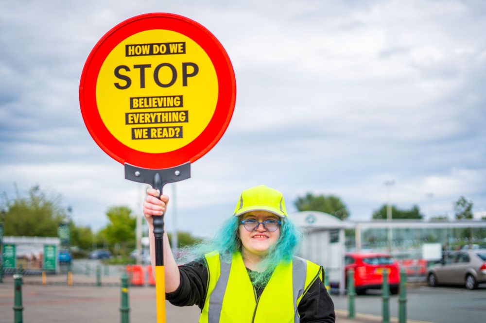 Artist Davina and three Changemakers stand at a crossroads, wearing yellow high-vis and lollipop sign.