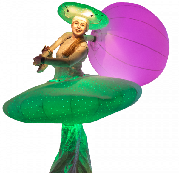 Cut-out image of a performer in a green lit up costume, carrying a purple lit balloon.