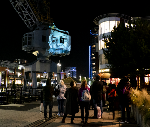 A picture of a woman is projected against a crane in the night sky.