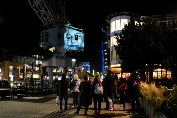 A picture of a woman is projected against a crane in the night sky.